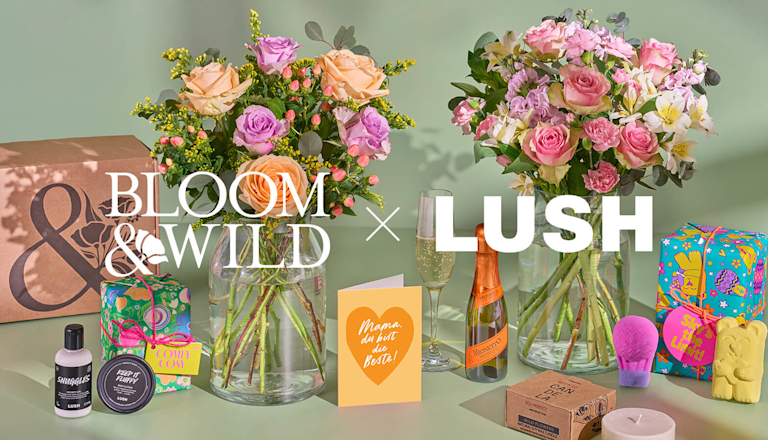Eine Szene in der bunt verpackte Badeprodukte von LUSH, zwei bunte Blumensträuße, ein Piccolo Sekt, eine Duftkerze und eine Muttertagskarte zu sehen sind. Auf dem Bild sind in weißer Schrift die Logos von Bloom and Wild und LUSH dargestellt. 