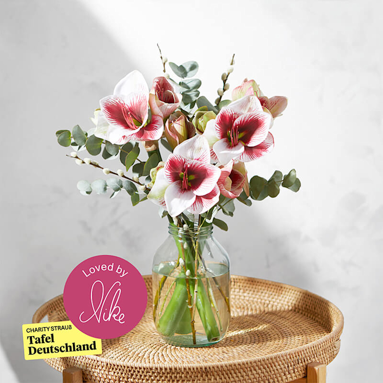 Ein blühender Blumenstrauß mit festlichen Rittersternen und Eukalyptusästen steht in einer Vase auf dem Beistelltisch. Daneben ist eine runde, cremefarbene Duftkerze zu sehen.