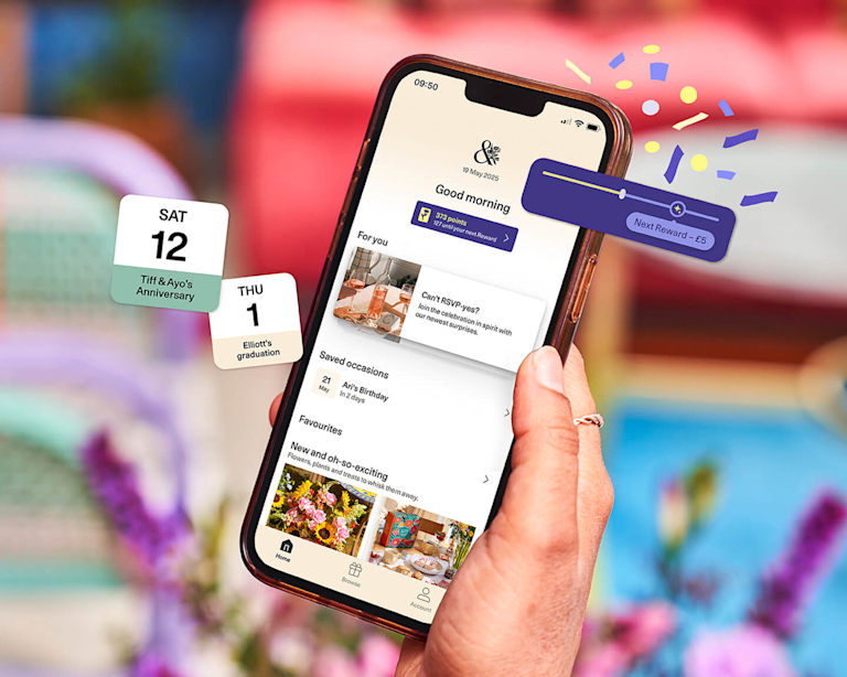 A hand holds a smartphone displaying the Bloom & Wild app. The screen shows 'Good morning', a 'Next Reward - £5' banner, and 'Saved occasions' including birthdays and anniversaries, with floating calendar reminders.