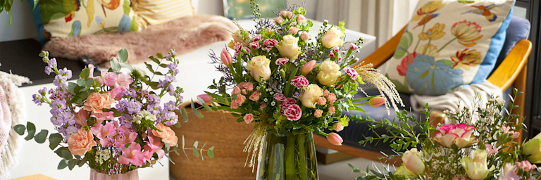 Three vibrant bouquets, lined with flowers like roses, carnations and stocks, in a homely setting. 
