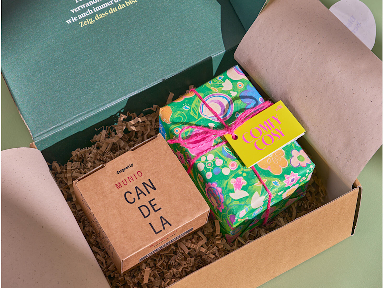 Eine Bloom and Wild Lieferbox in der ein schön verpacktes LUSH Geschenkset und eine verpackte Duftkerze zu sehen sind.