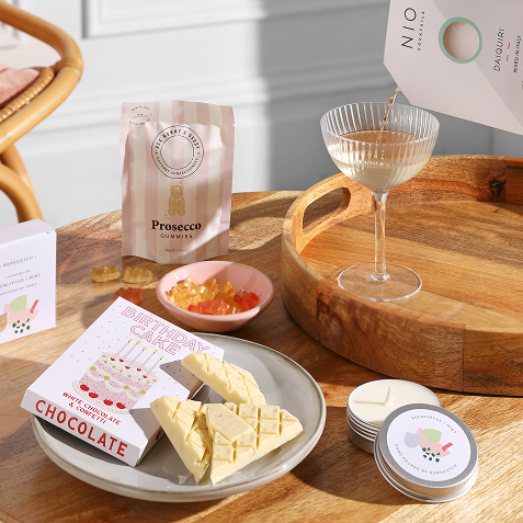 A selection of hamper items including a candle, birthday cake chocolate, a cocktail mix, and gummy bears. 