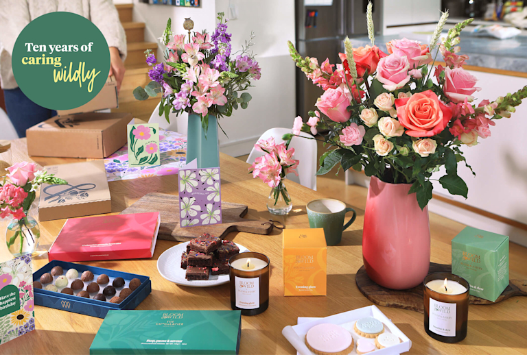A group shot of all the decade of Bloom & Wild products laid out on a table. There are flowers, candles, chocolates, brownies and greetings cards.