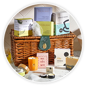 A wicker gift hamper filled with assorted skincare and wellness products, including boxed items, a candle, tea etc. 