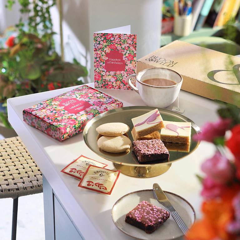Delicious treats and tea arranged in a Bloom & Wild gift box. Includes gooey brownies, buttery biscuits, and fragrant tea, alongside a floral card and gold spoon.  Perfect for a thoughtful pick-me-up.