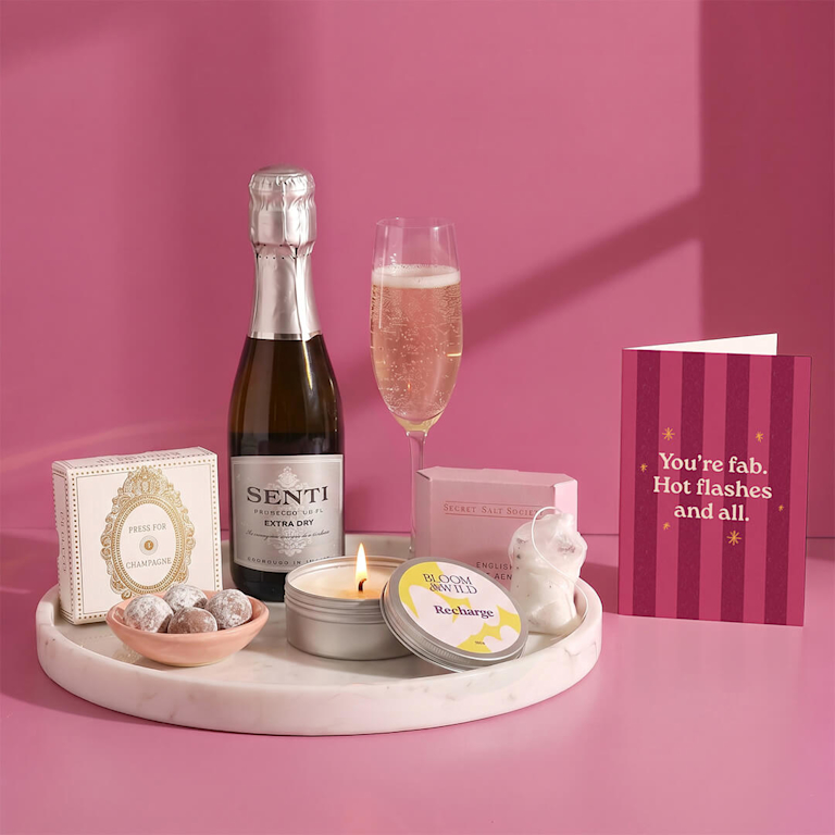 Pamper tray featuring crisp Senti prosecco, a glowing scented candle, rich chocolate truffles, and a supportive card reading "You're fab. Hot flashes and all."
