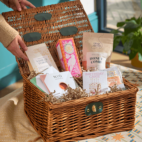 Open wicker hamper filled with vanilla fudge, chocolates, honeycomb, notecards and a "Birthday Cake" greeting card, nestled in shredded paper.