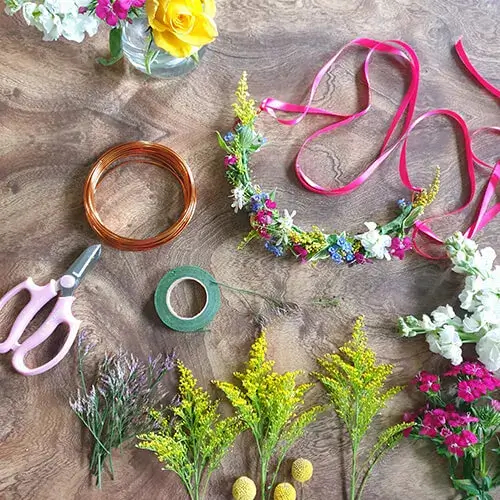 Scissors, wire, tape and flowers lay on a wooden table.