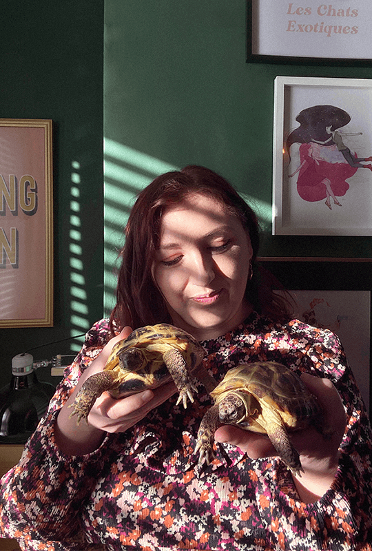 Alice, a light-skinned woman with reddish-brown hair, cradles two tortoises.