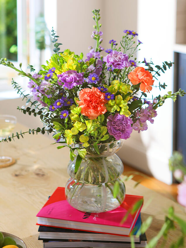Eine Vase mit bunten Blumen auf einem Stapel Bücher