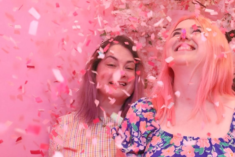 Tara and Kezia smile as pink confetti rains down on them.