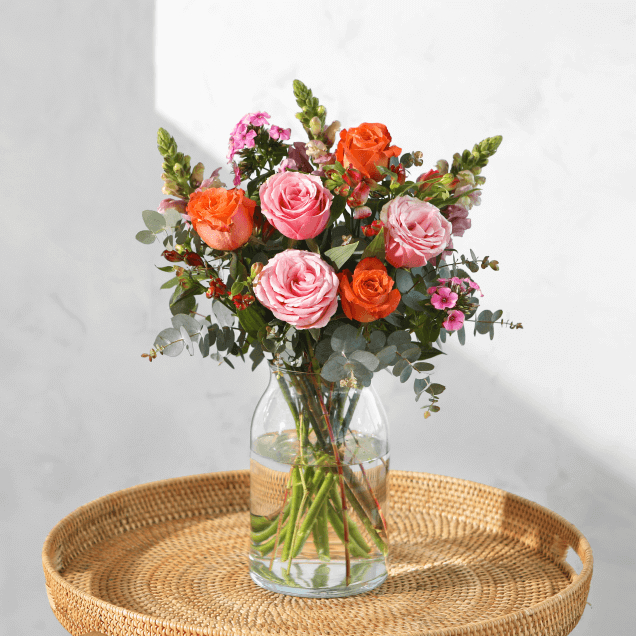 The Elaine timeless bouquet by Bloom & Wild arranged in a glass vase, featuring pink and red roses and a variety of green stems