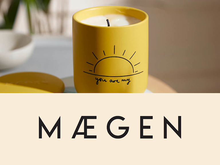 A yellow candle is captured in the afternoon sunlight. The candle has a sun illustration on it, with text written beneath it that reads 'You are my'. Beside this image is Maegen's logo, which sits on a linen background.