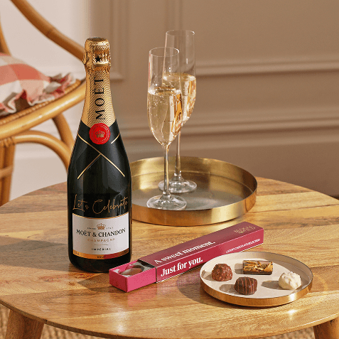 Bottle of Moët & Chandon champagne with two filled flutes on a gold tray, next to a pink box of chocolate truffles labelled "Just for you.
