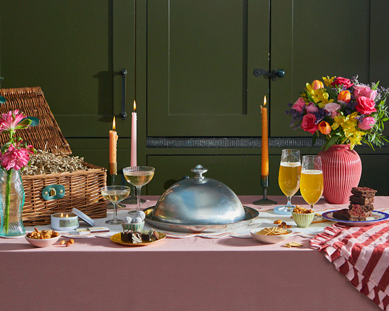 An animated Valentine's spread featuring a vibrant bouquet, stacked brownies, and flickering candles. A silver cloche lifts to reveal a romantic gift, evoking a fragrant, joyful, and indulgent mood.