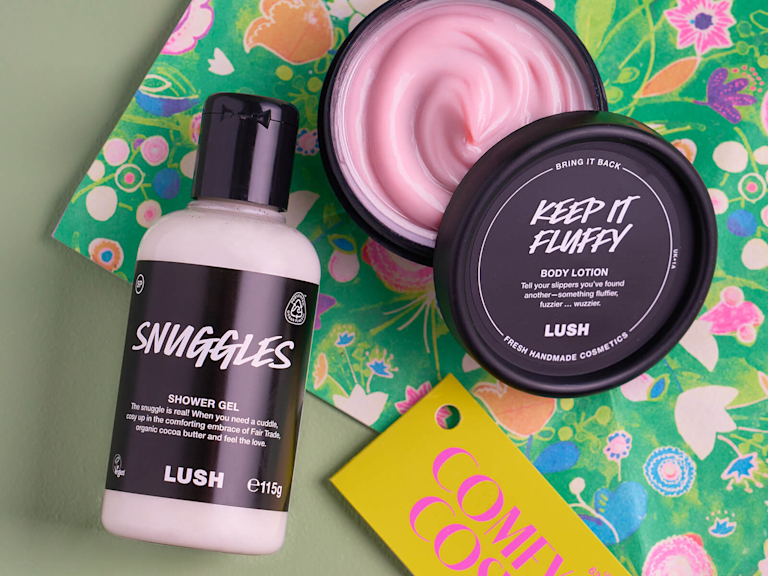 Ein Geschenkset bestehend aus einem Duschgel und einer cremigen, halb geöffneten Bodylotion von LUSH liegen auf einer blumig bunten Geschenkverpackung