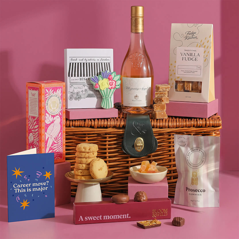 Luxe wicker hamper packed with rose wine, vanilla fudge, artisanal chocolates, iced biscuits, prosecco gummies, and a card reading "Career move? This is major".