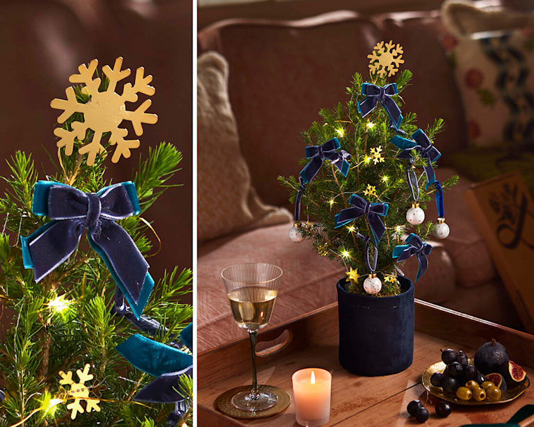 A miniature Christmas tree, decorated with snowflakes and bows. A Christmas card is on the table next to it. 