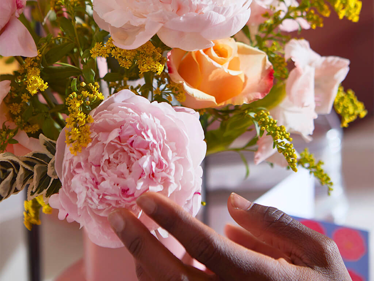 A collage of three images, showing a series of snapshots around a dresser. There's a pink peony bouquet on the dresser and post-its with affirmations on the mirror. A man with a rainbow flag sits in front of them, smiling.