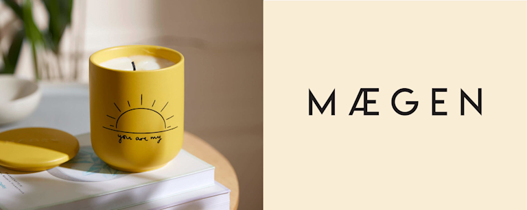 A yellow candle is captured in the afternoon sunlight. The candle has a sun illustration on it, with text written beneath it that reads 'You are my'. Beside this image is Maegen's logo, which sits on a linen background.