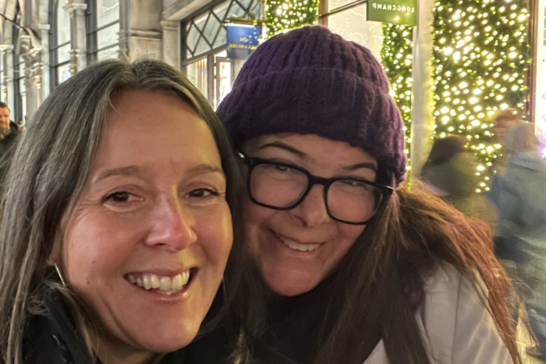 Jude and Gemma smile at the camera, high-street fairy lights twinkling in the background.