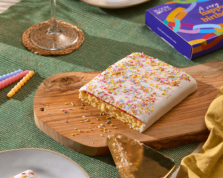 A letterbox shaped birthday cake with white icing, jam, and sprinkles on top.