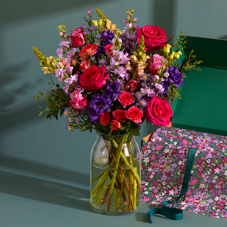 A pink vase containing a vibrant bouquet of purple, pink and orange flowers sits on a kitchen counter.