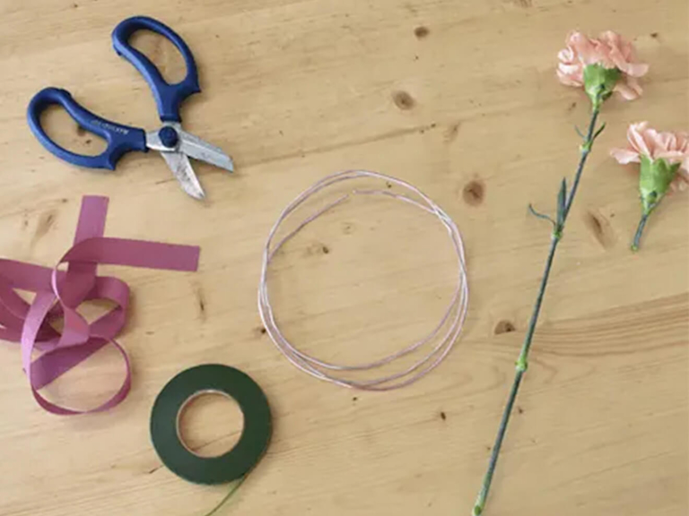 Eine Floristenschere, Seidenband, ein Blütenstiel, Draht und Klebeband liegen auf einem Holztisch