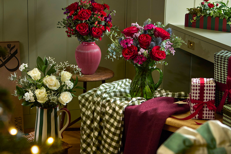 Three Christmas bouquets of red and white roses in vases, surrounded by wrapped presents and fairy lights