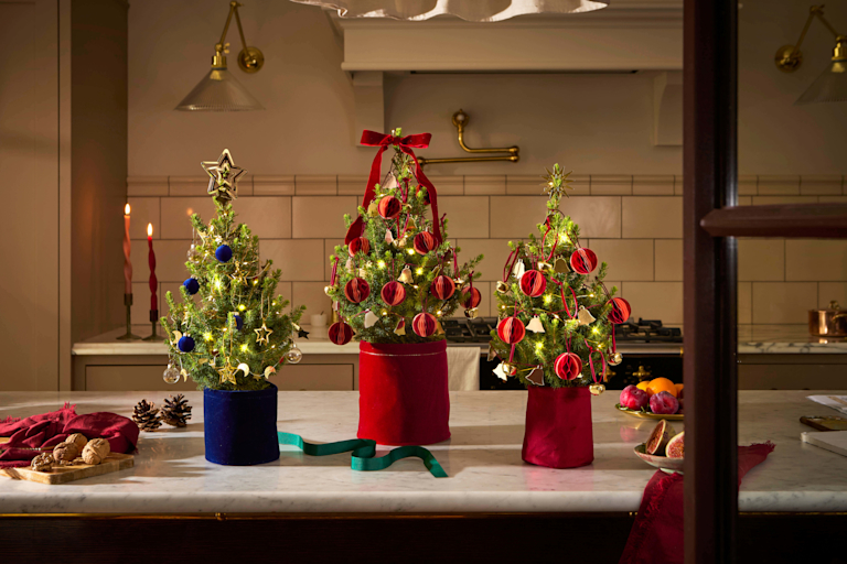 Eine Auswahl an festlich geschmückten Mini-Mini-Weihnachtsbäumen mit jeweils verschiedenen und originellen Ornamenten als Baumschmuck, darunter Schneemänner, Strohsterne und goldene Glöckchen.