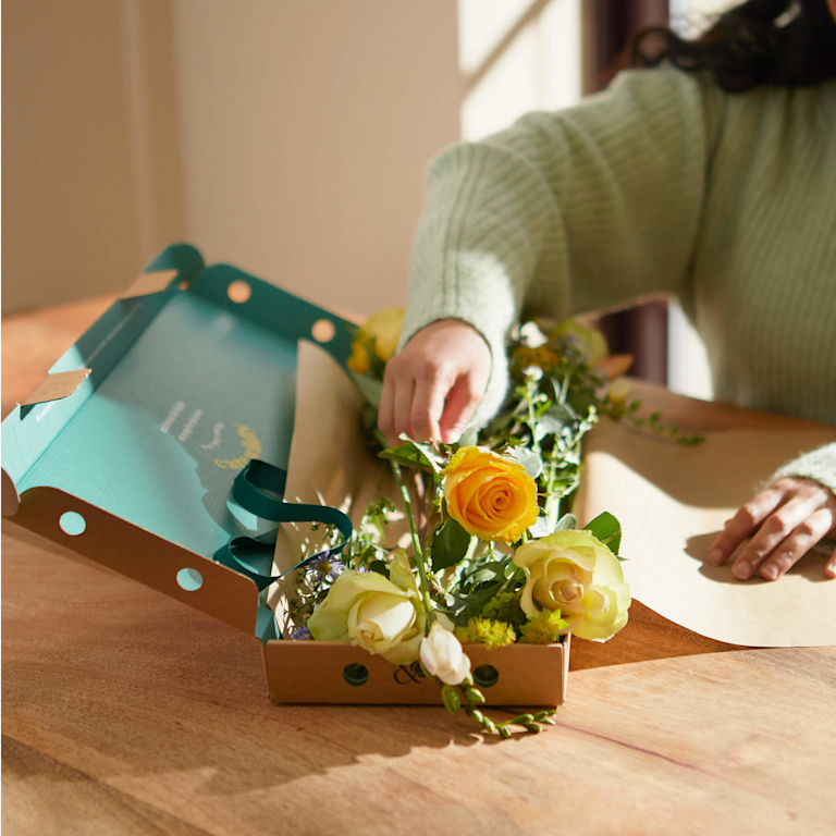 A woman carefully picking out yellow roses from a Bloom & Wild subscription box.