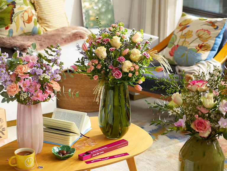 Three vibrant bouquets, lined with flowers like roses, carnations and stocks, in a homely setting. 