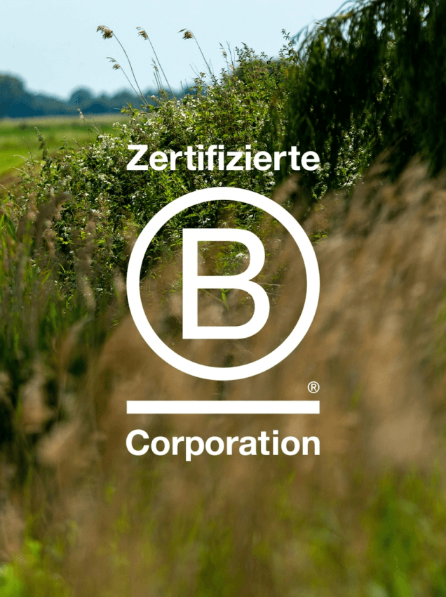 Das offizielle B Corp® Logo auf dem Foto einer ländlichen Hecke
