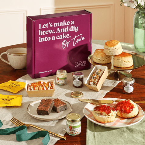 Bloom & Wild "Afternoon Tea for Two" box on a table with scones, jam, clotted cream, brownies, tea bags and a scone spread with jam.