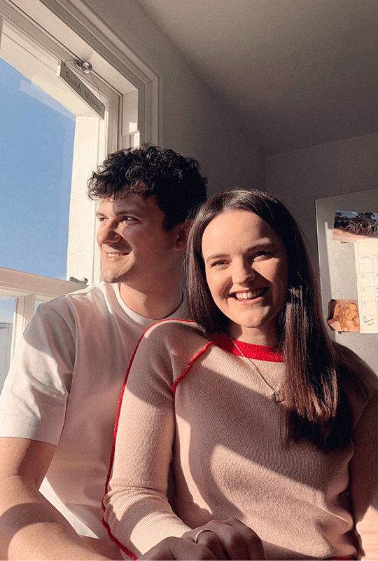 Georgia and Josh sit on a kitchen window sill, sunlight pouring through and illuminating them.