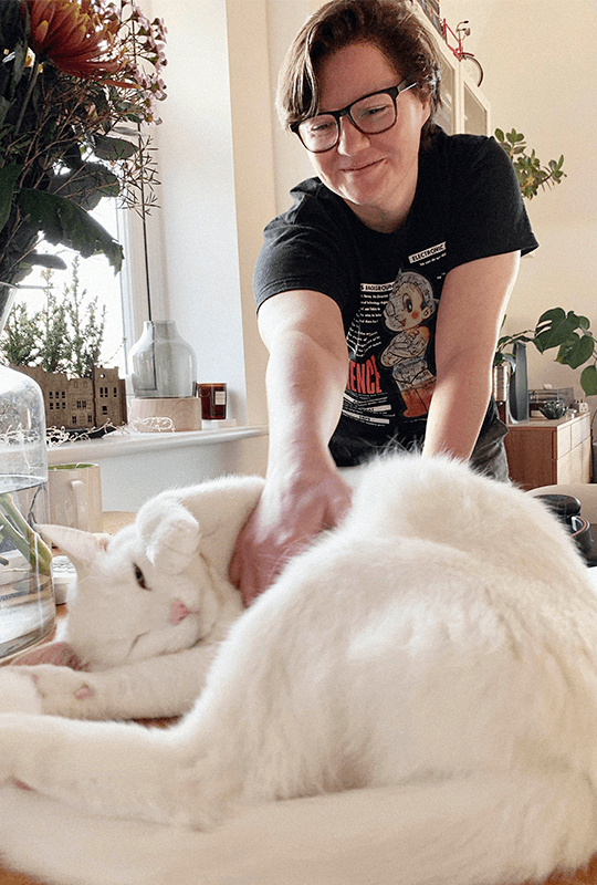 Marta reaches forwards and tickles the tummy of a large white cat.