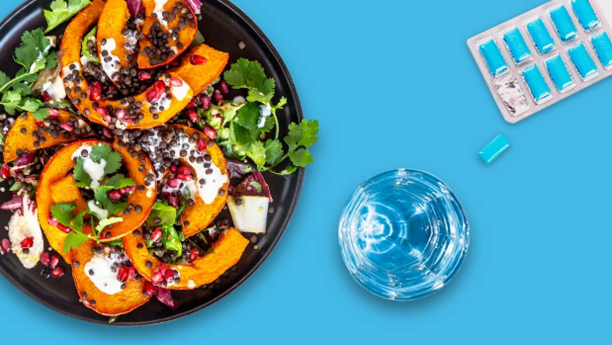 Plate with healthy salad, a glass of water, and blister package gum with one piece popped out