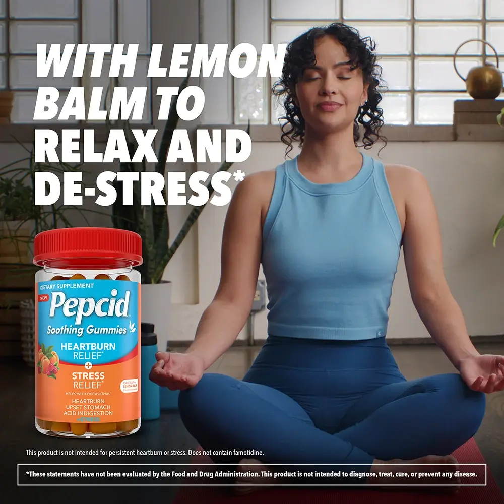 Woman meditating in a lotus position on a red mat, next to Pepcid gummies, promoting heartburn and stress relief, with house plants in the background.