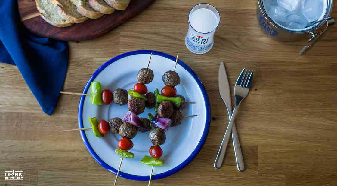 there are a plate of meatballs and vegetables on skewers on a table