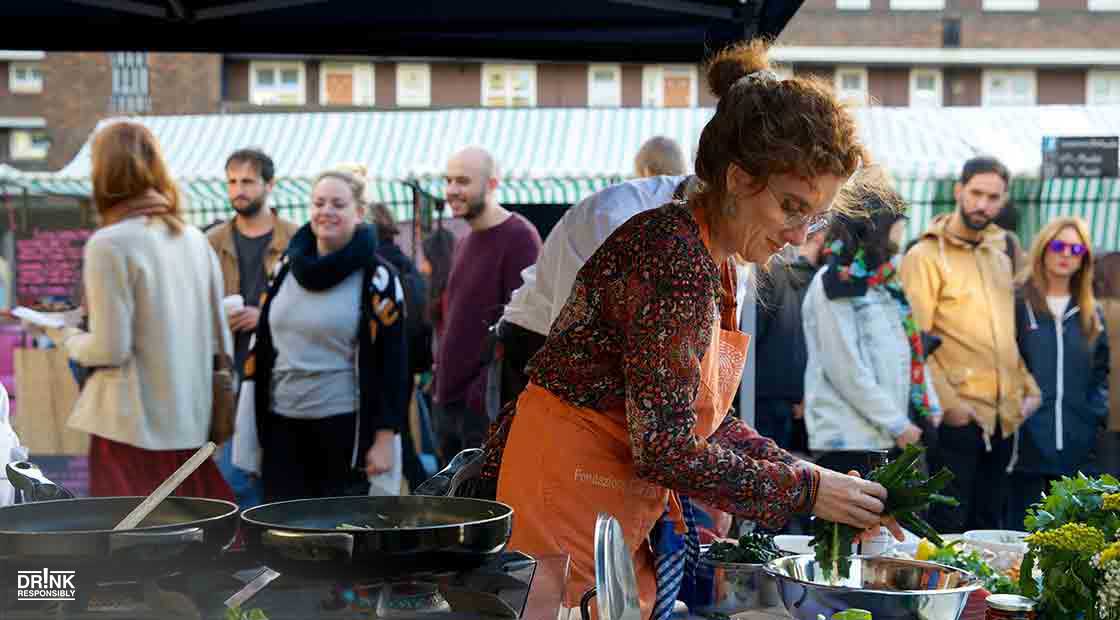 woman preparing food at outdoor market with crowd of people watching
