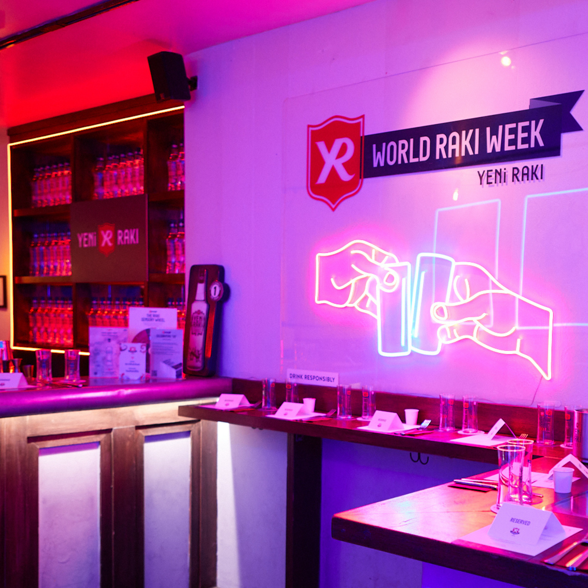 A lively bar scene with a "World Raki Week" neon sign, featuring Yeni Raki bottles on shelves and tables ready for tasting the Turkish spirit.