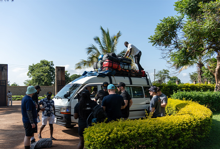 Several men helping to pack a mini bus with lots of luggage