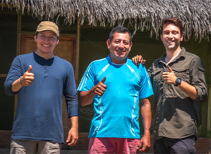 Dael [right] poses for a picture with a local. There are three men in the image all posing with a thumbs up and similing.