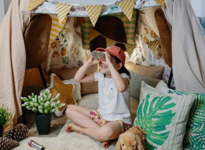 Little girl playing with cardboard binoculars while camping at home in the living room