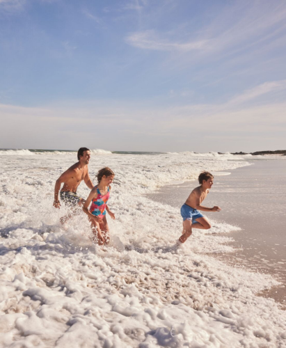 A man and two children running in the sea along the beach.