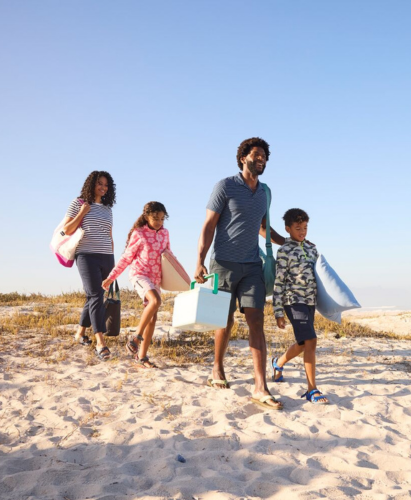 A man and two children running in the sea along the beach.