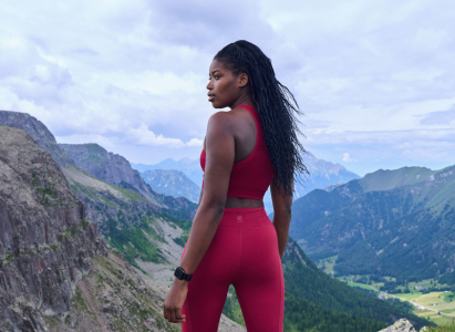 woman wearing a red sports bra and leggings, stood in front of a mountainous back ground