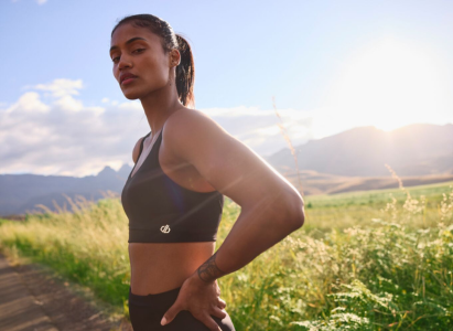 woman wearing a black sports bra, her hands are on her hips and she is stood infront of a field