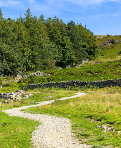 Winding gravel hiking trail leading uphill on Gowbarrow Fell in the Lake District.