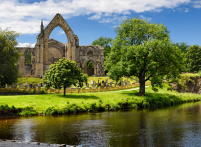 12th century Augustinian Bolton Priory church ruins on the River Wharfe with stepping stones at Bolton Abbey, Wharfedale, North Yorkshire, England